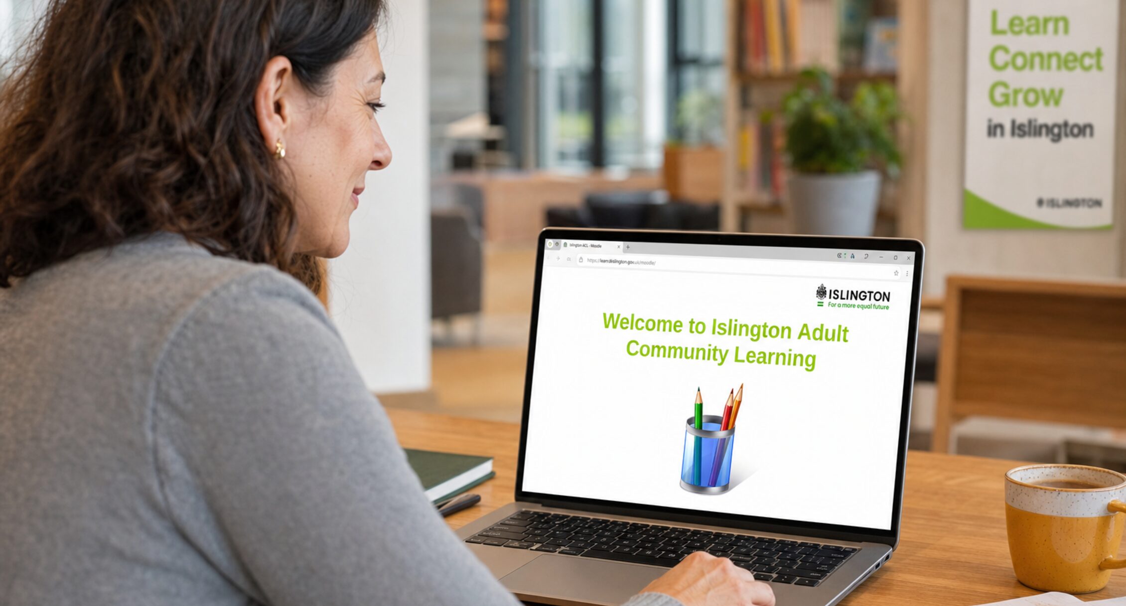 An adult community learner in a bright Islington learning centre looking at a laptop showing the green-branded Welcome to Islington Adult Community Learning Moodle page.